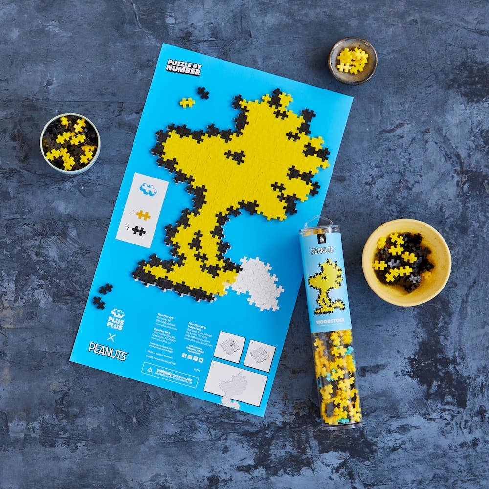 Peanuts-themed puzzle with completed pieces on a blue sheet, surrounded by small bowls of puzzle pieces on a dark gray surface.