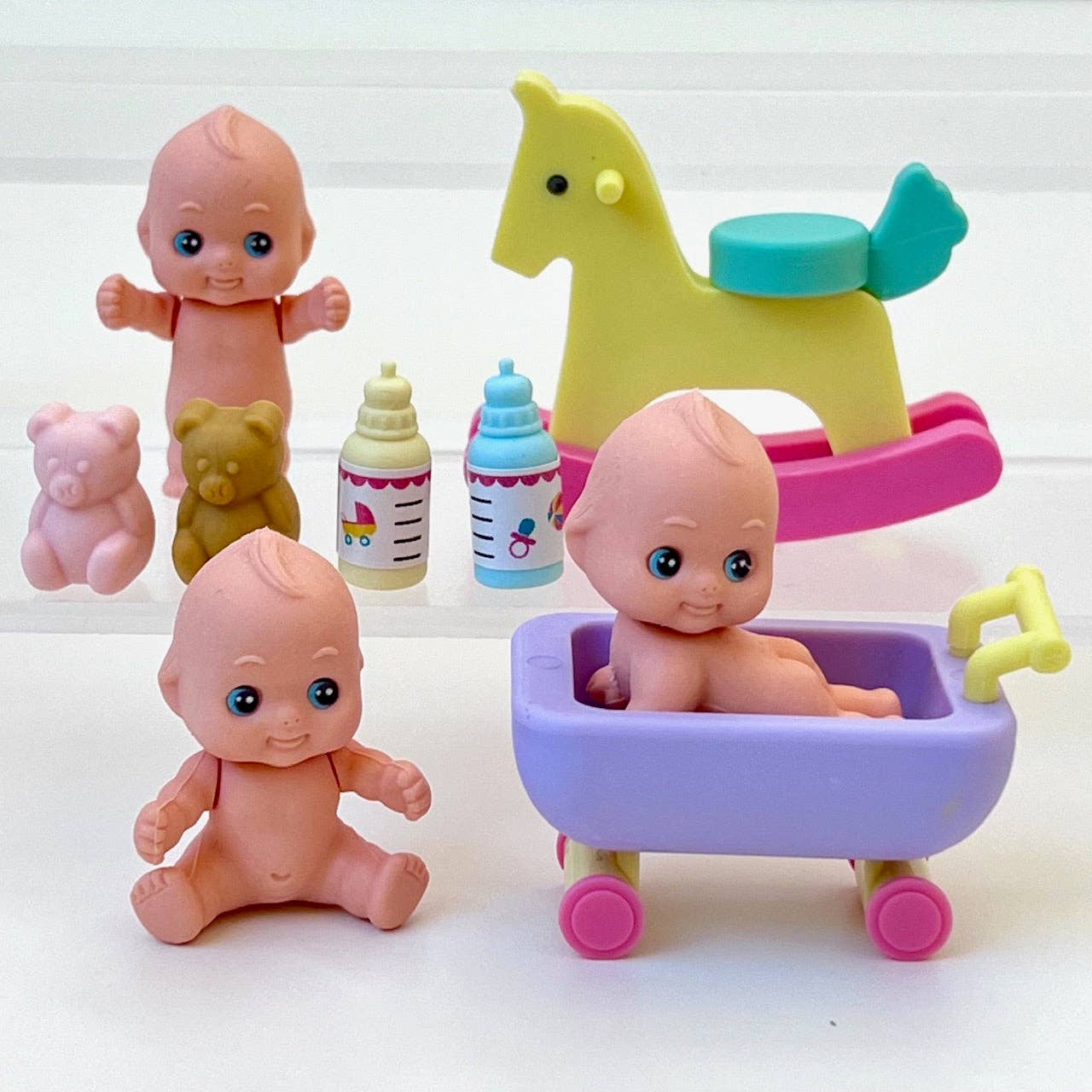 Set of toy baby erasers and toys including a rocking horse, bottles, and a bathtub on a white background
