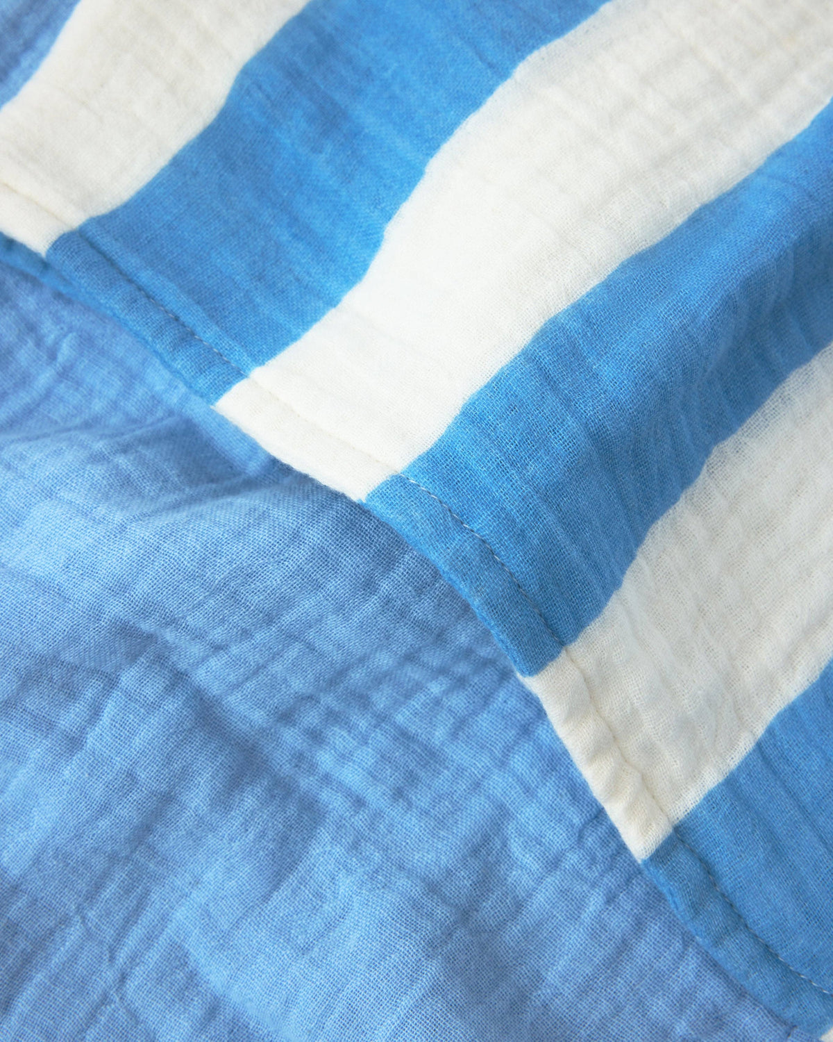 A close-up of a crinkled gauze fabric with alternating blue and white stripes, showing the texture and stitching detail.