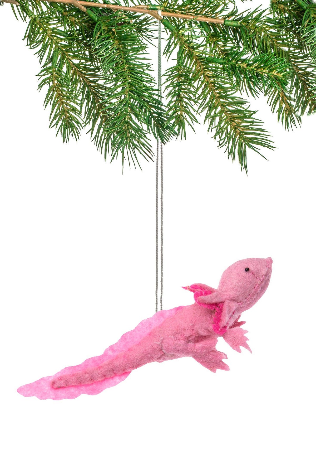 A pink felt axolotl Christmas ornament hanging from a green pine tree branch against a white background.