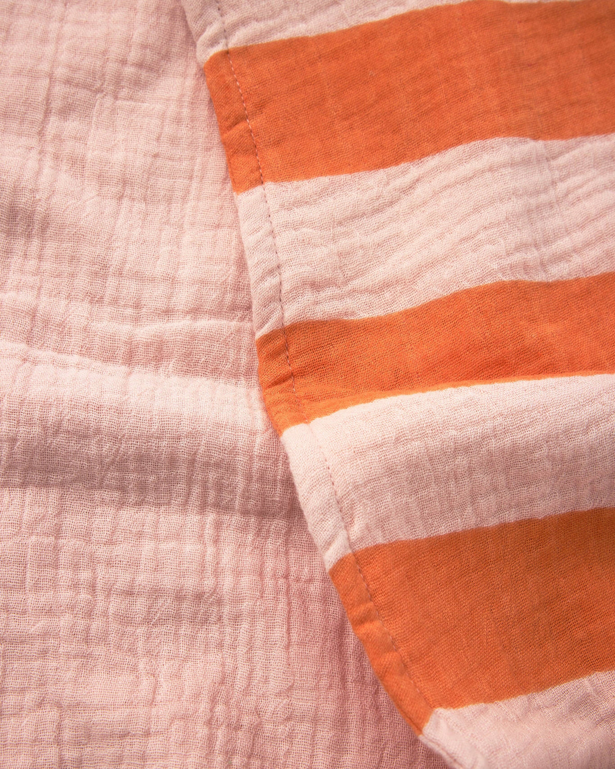 A close-up of a crinkled gauze textile with alternating horizontal stripes in soft blush pink and bright orange.