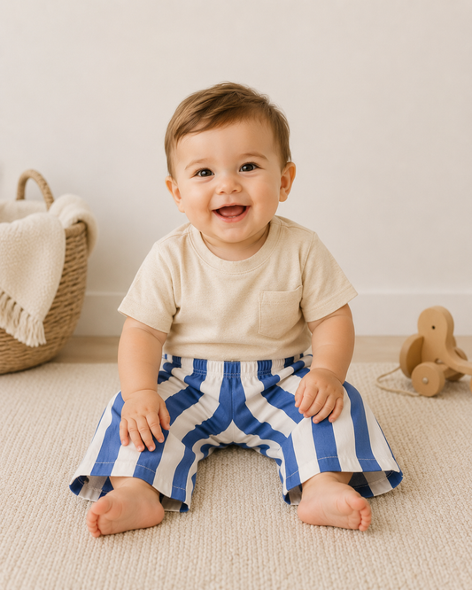 Baby sitting on a carpeted floor wearing blue and white striped pants.