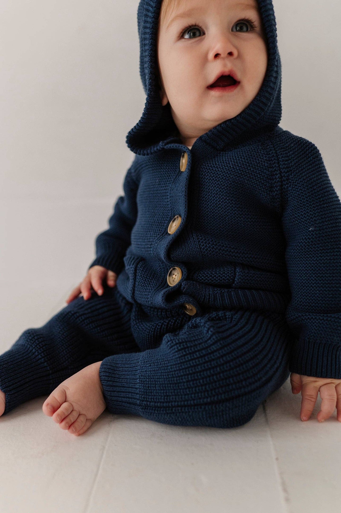 Baby wearing a navy blue knitted outfit with buttons on a light background