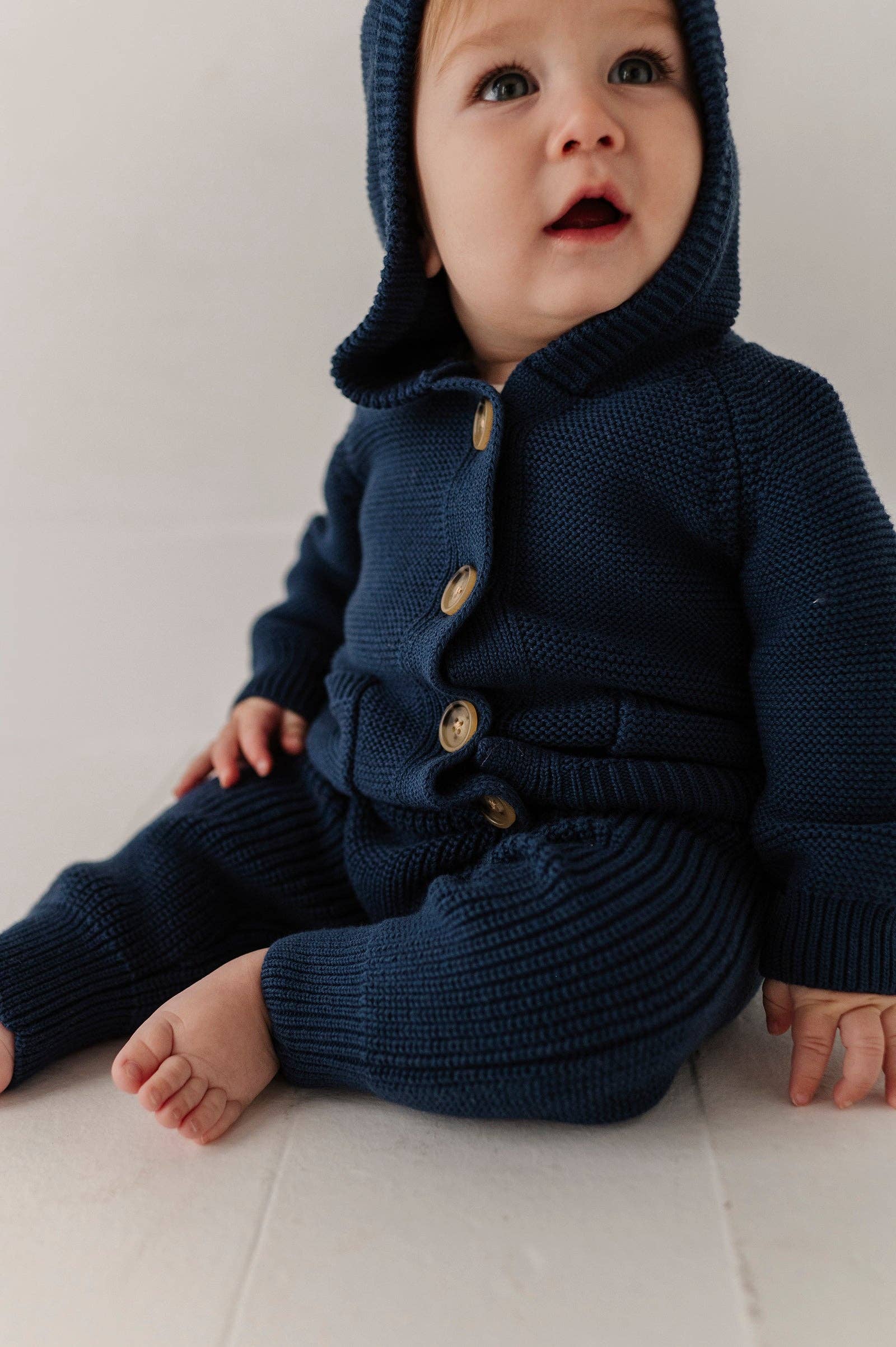 Baby wearing a navy blue knitted outfit with buttons on a light background