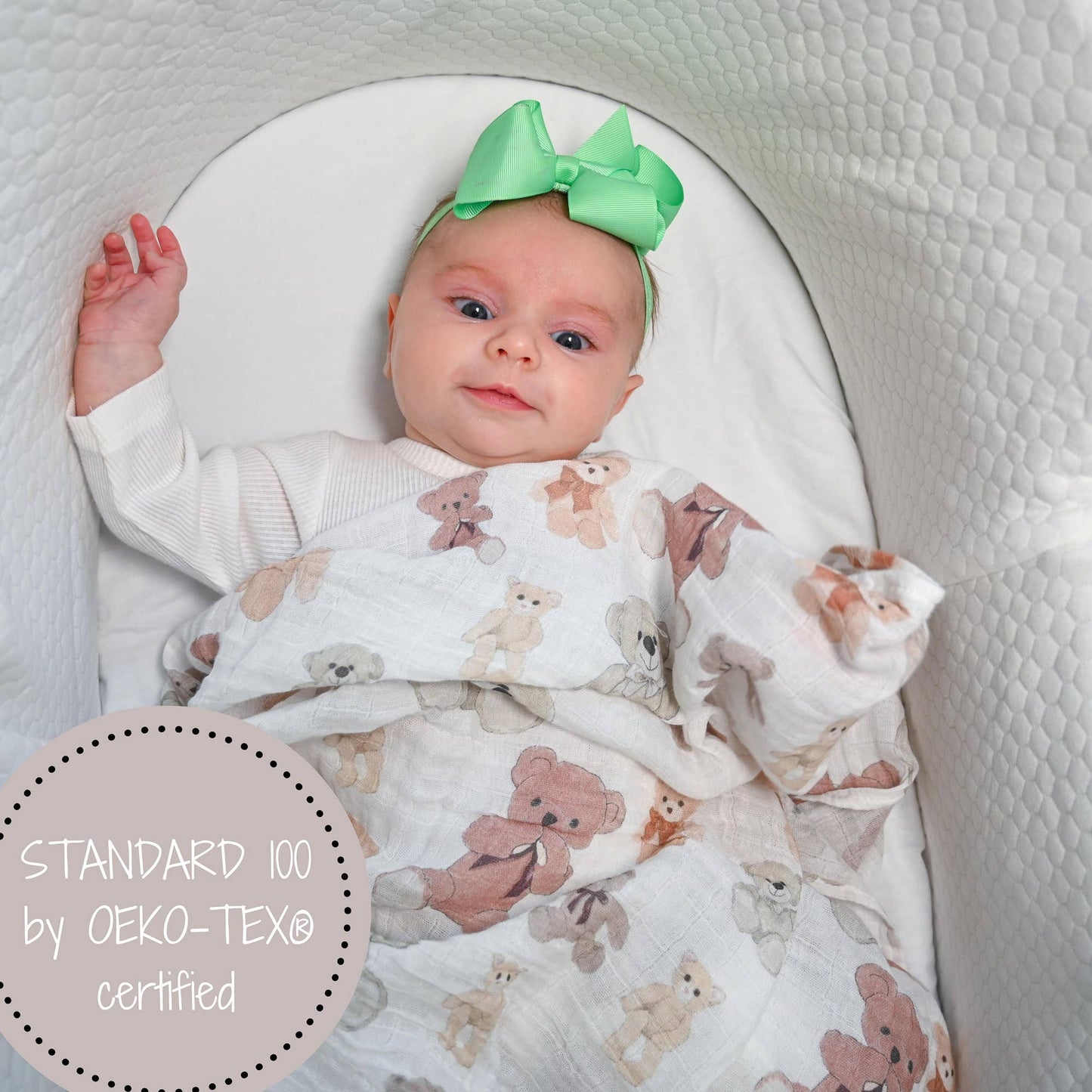 Baby wrapped in a blanket with teddy bear pattern, wearing a green bow headband, in a crib.