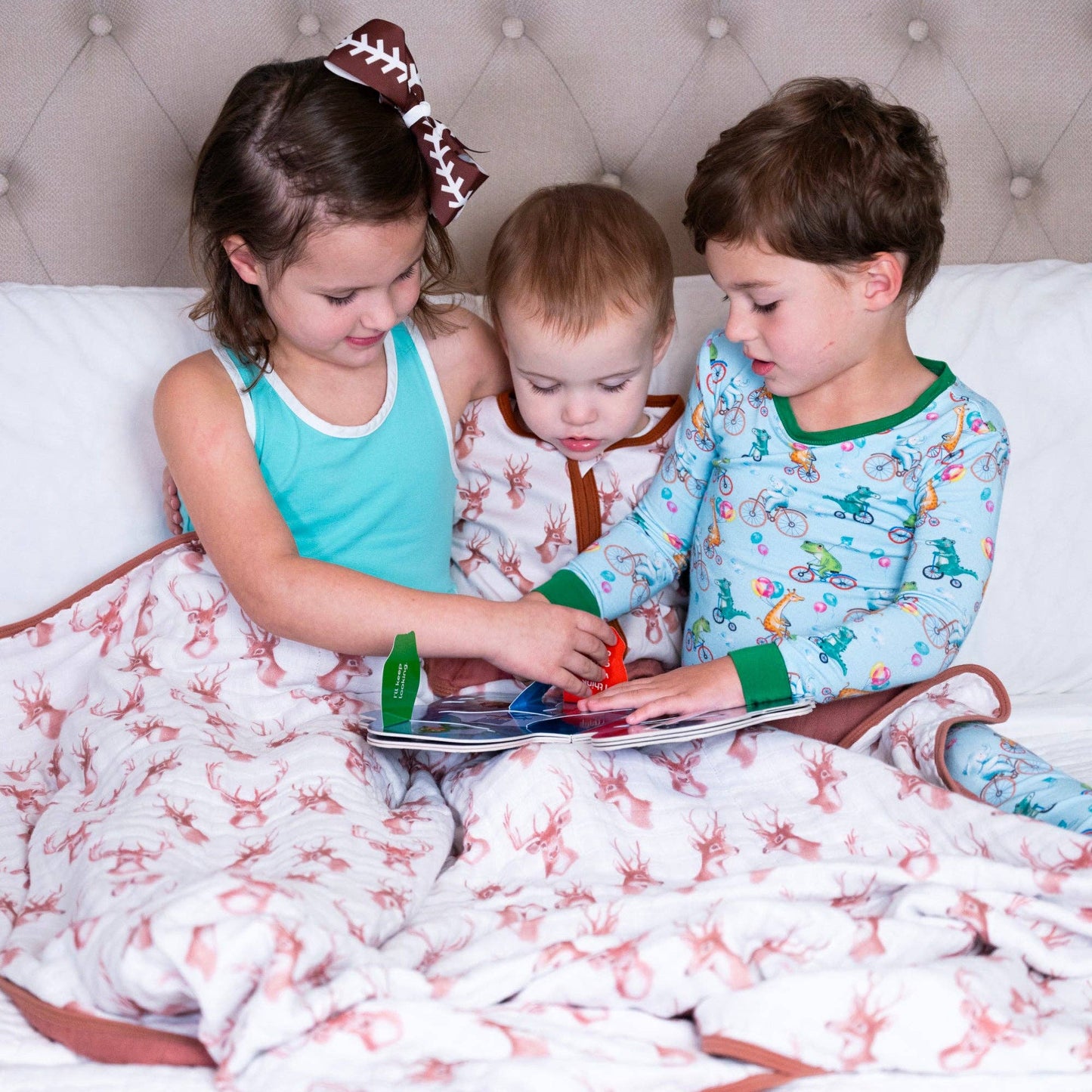 Three children sitting on a bed, reading a book together.