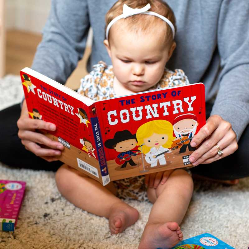 Person reading 'The Story of Country' book to a child on a carpeted floor.