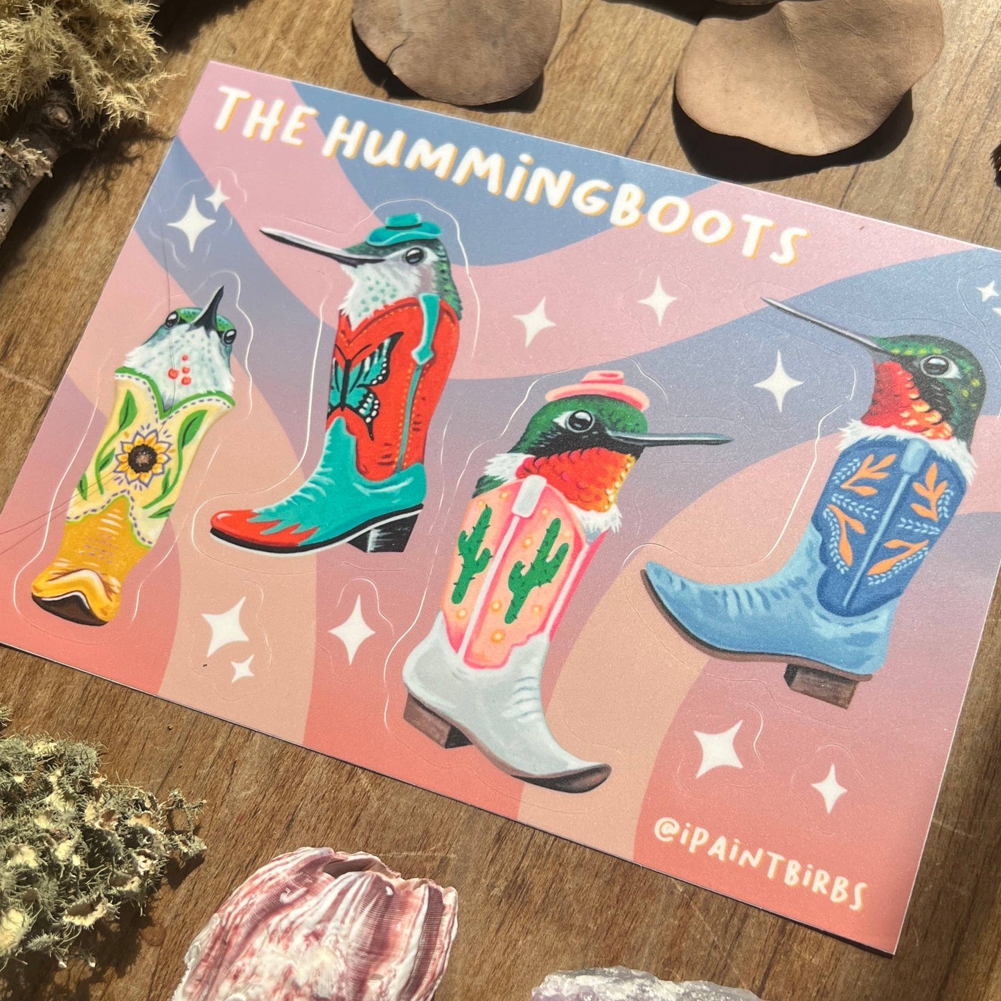 Illustrated sticker sheet of boots and hummingbirds with 'The Hummingboots' branding on a wooden surface.