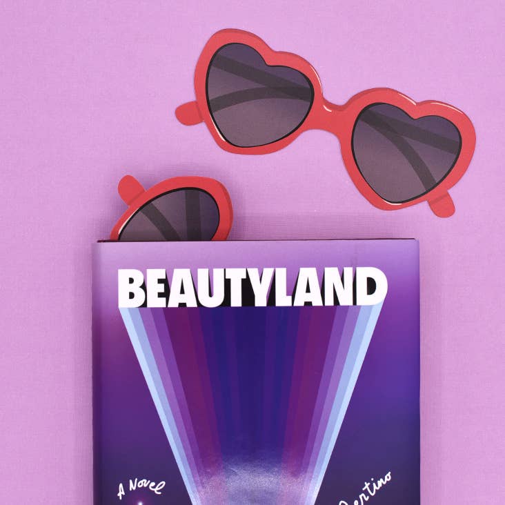 Heart-shaped sunglasses on a 'Beautyland' book against a pink background