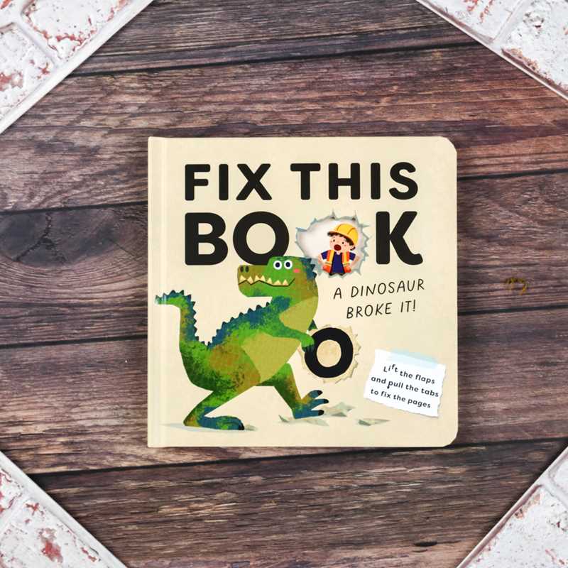 Children's book titled 'Fix This Book' with a dinosaur illustration on a wooden surface