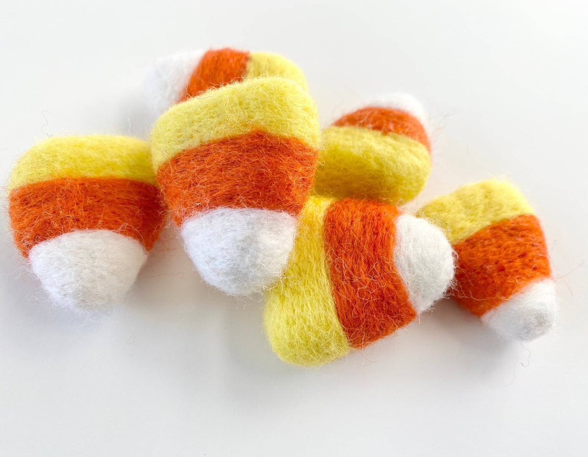 Four felted wool candy corn decorations with yellow, orange, and white stripes on a plain white background.