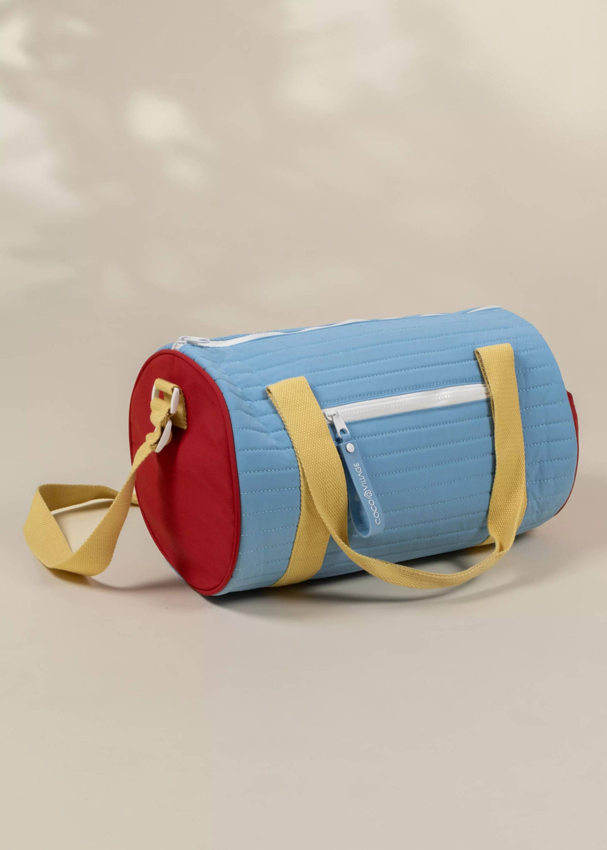 Colorful cylindrical bag with a red bottom, blue top, and yellow straps on a beige background