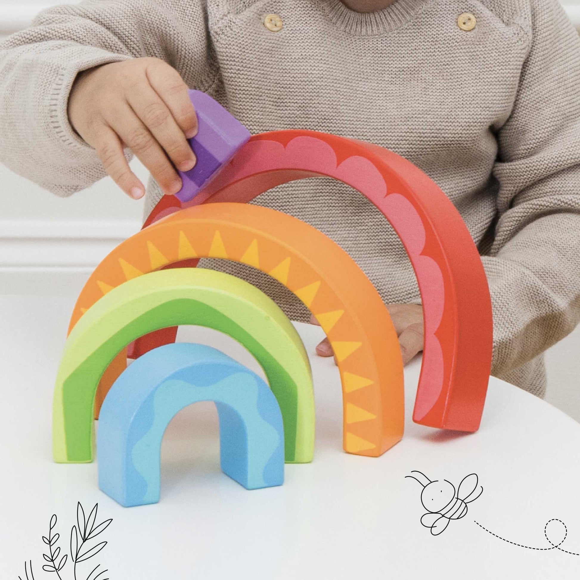 Child playing with colorful wooden arch toys on a white surface