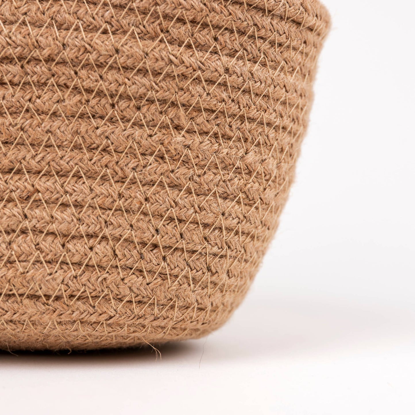 Close-up of a woven natural fiber basket in a warm tan color, showing the detailed braided texture against a clean white background.