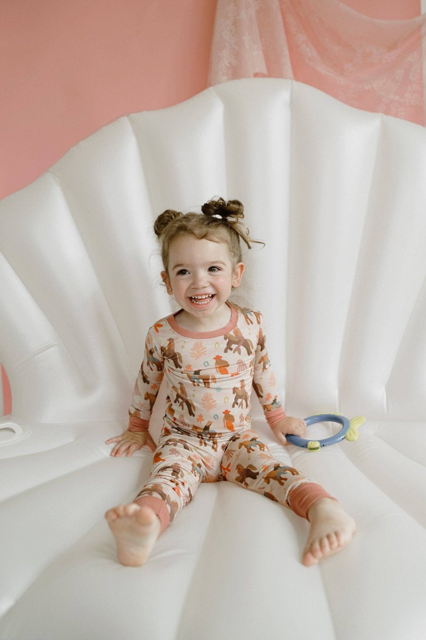 Child wearing patterned pajamas sitting on a white blanket with a pink background