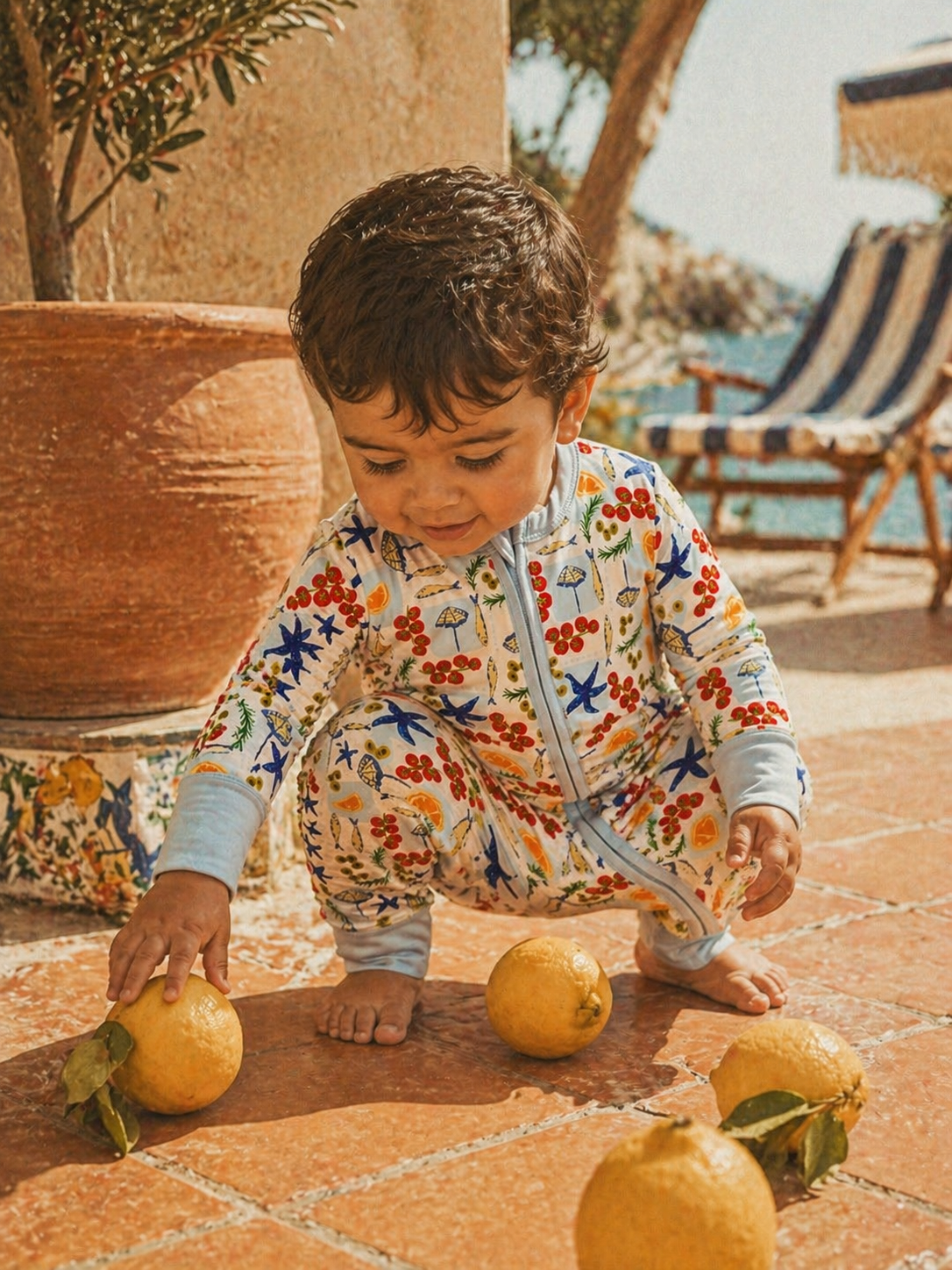 Child in a colorful pajama playing with lemons on a tiled floor outdoors.