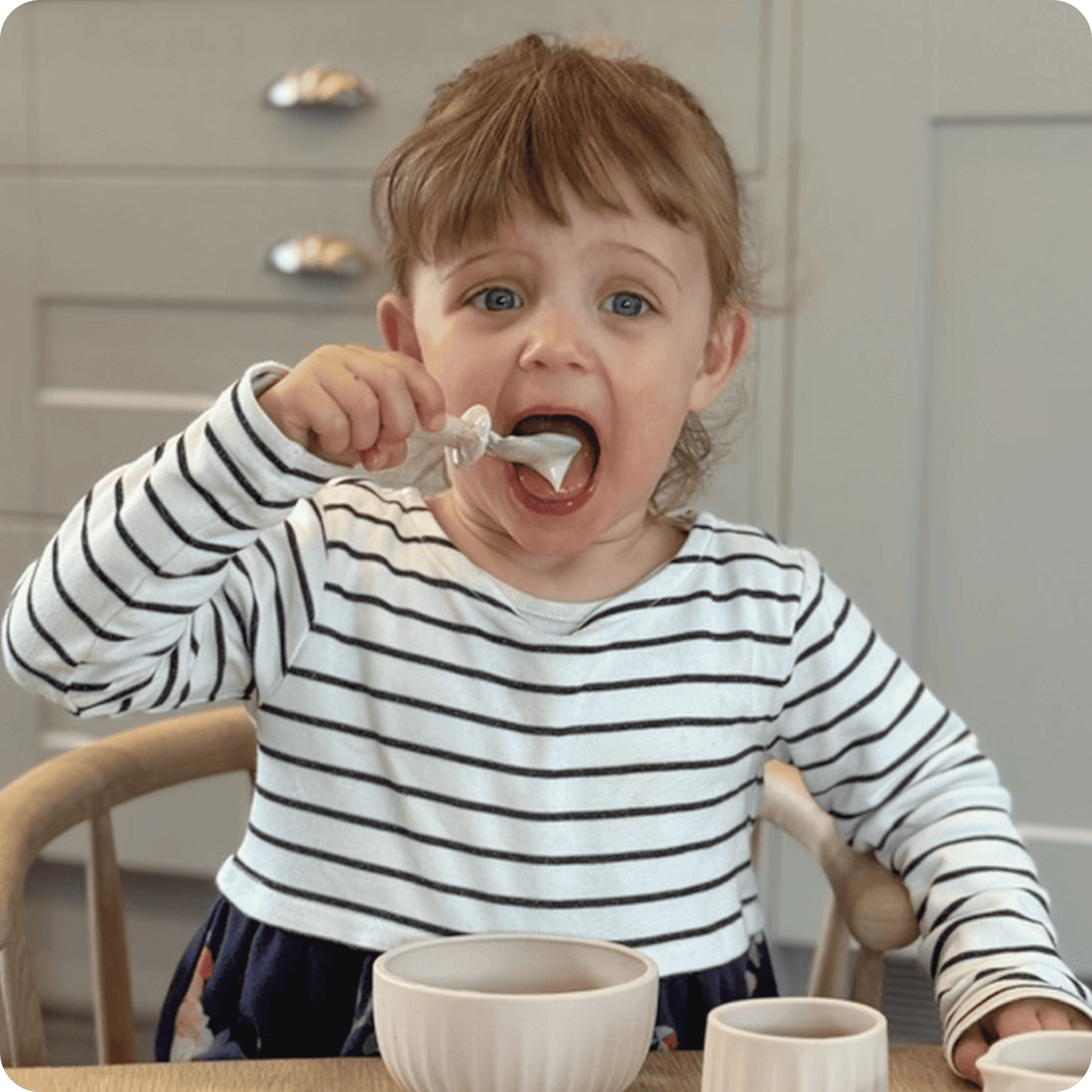 Child eating with a spoon in a kitchen setting
