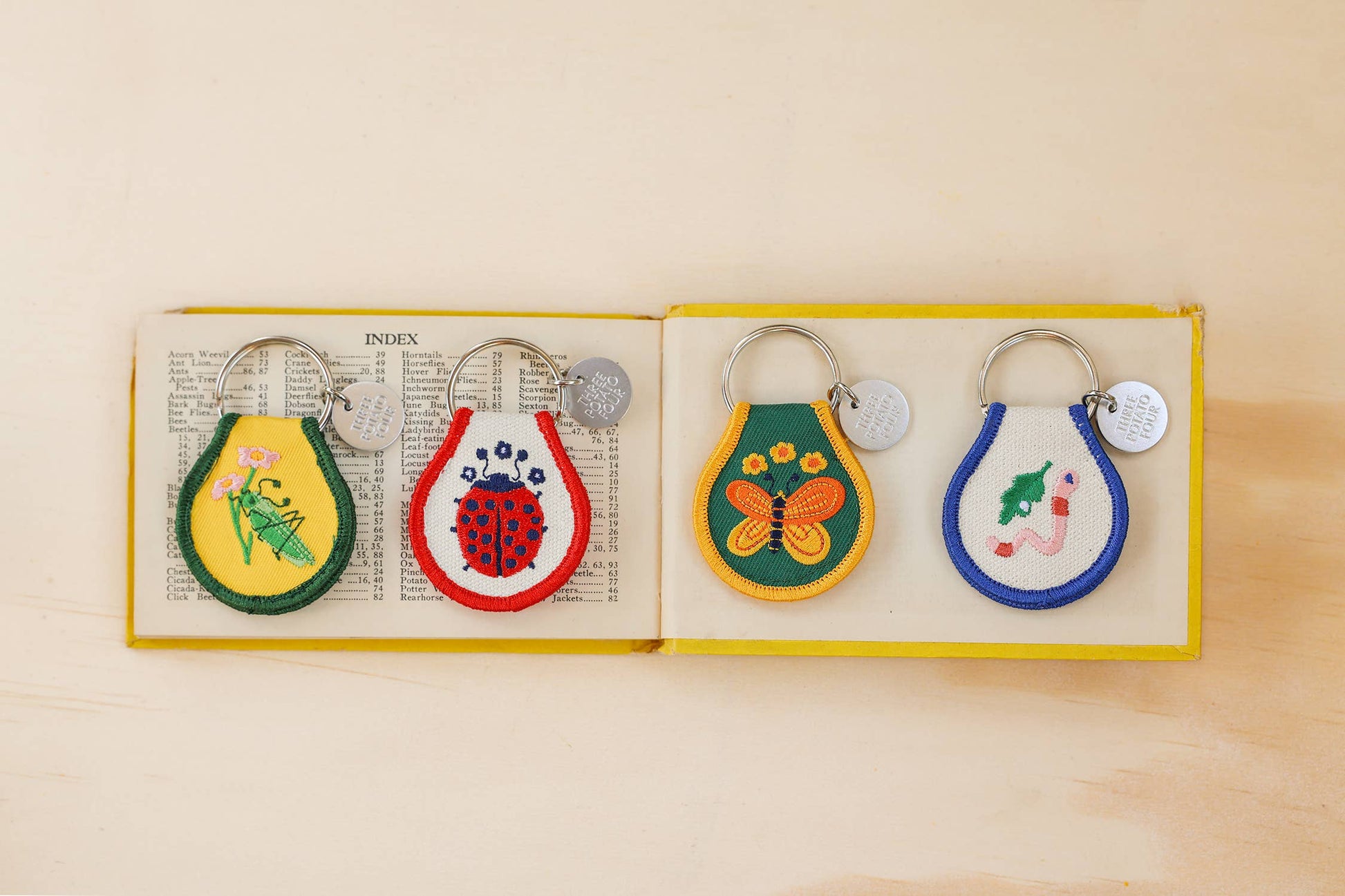Set of colorful keychains with insect designs in a box on an open book.
