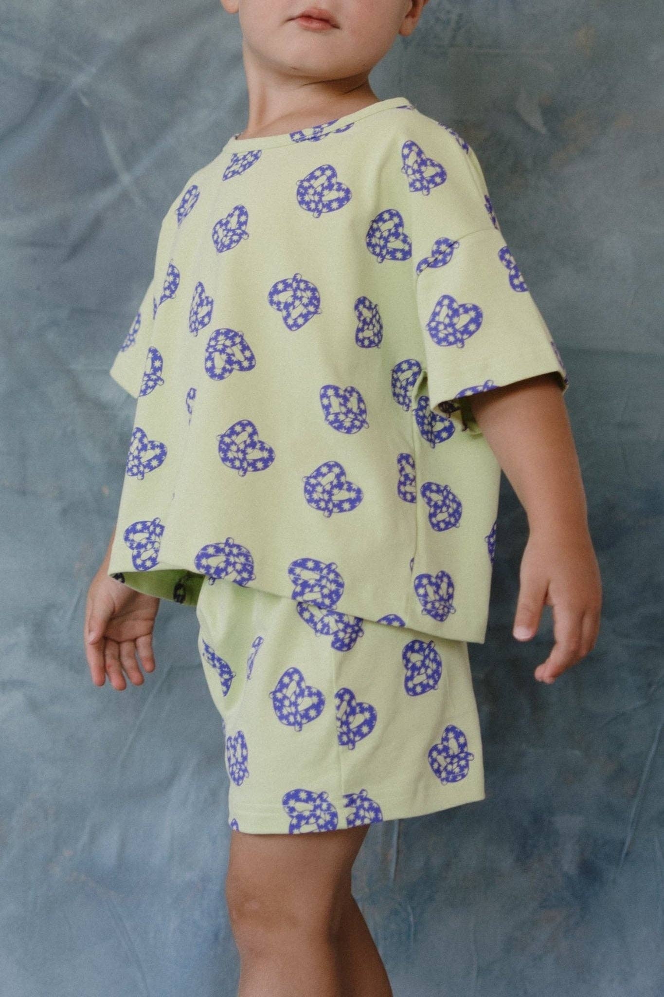 Child wearing a light green outfit with blue pretzel patterns on a gray background