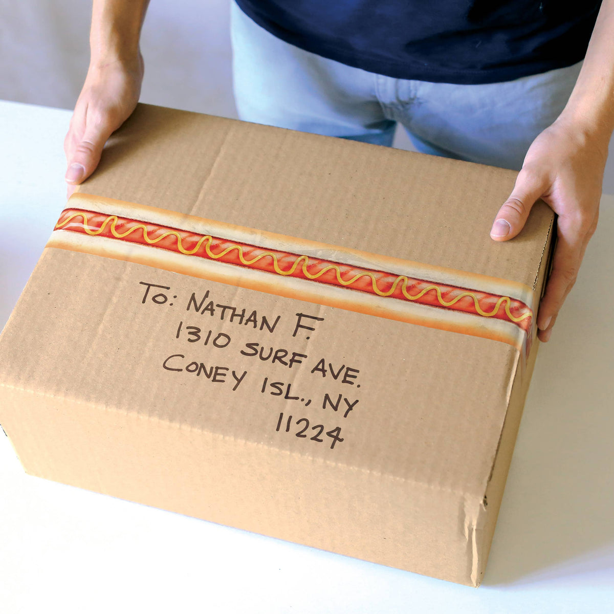 Cardboard box with hot dog-themed wrapping and address label, held by a person.