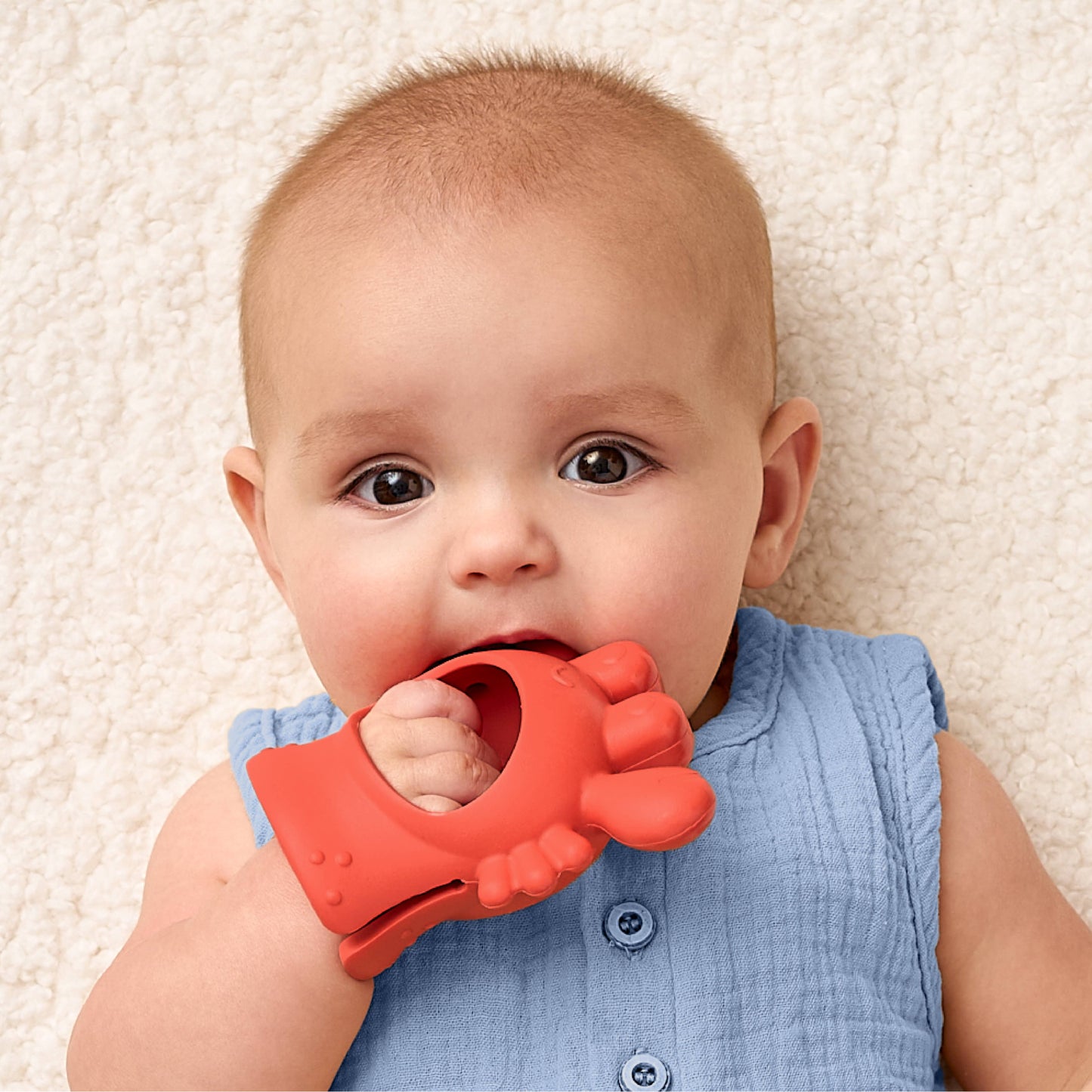 Baby holding a red teething toy on a beige carpet