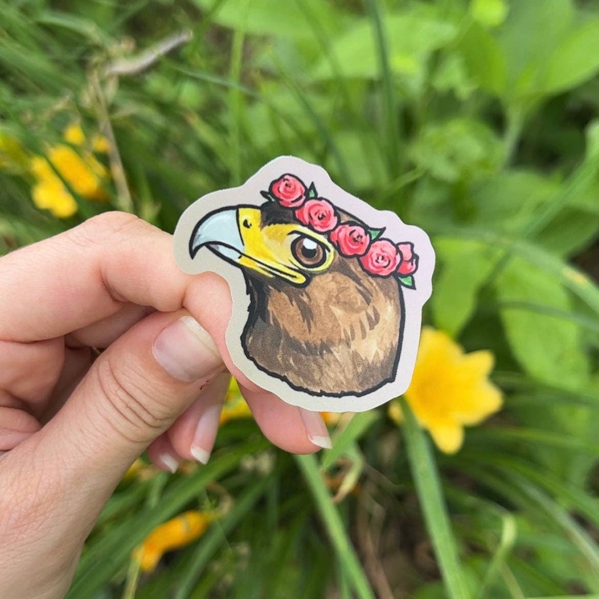 Hand holding a sticker of a bird with a flower crown against a natural background