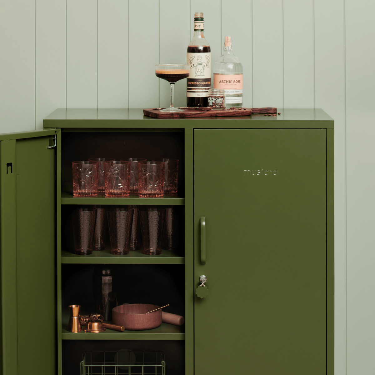 Green cabinet with bar items on a wooden surface against a light green wall.