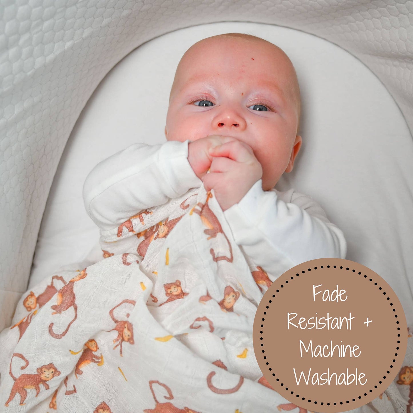Baby wrapped in a blanket with monkey pattern, lying on a white surface.