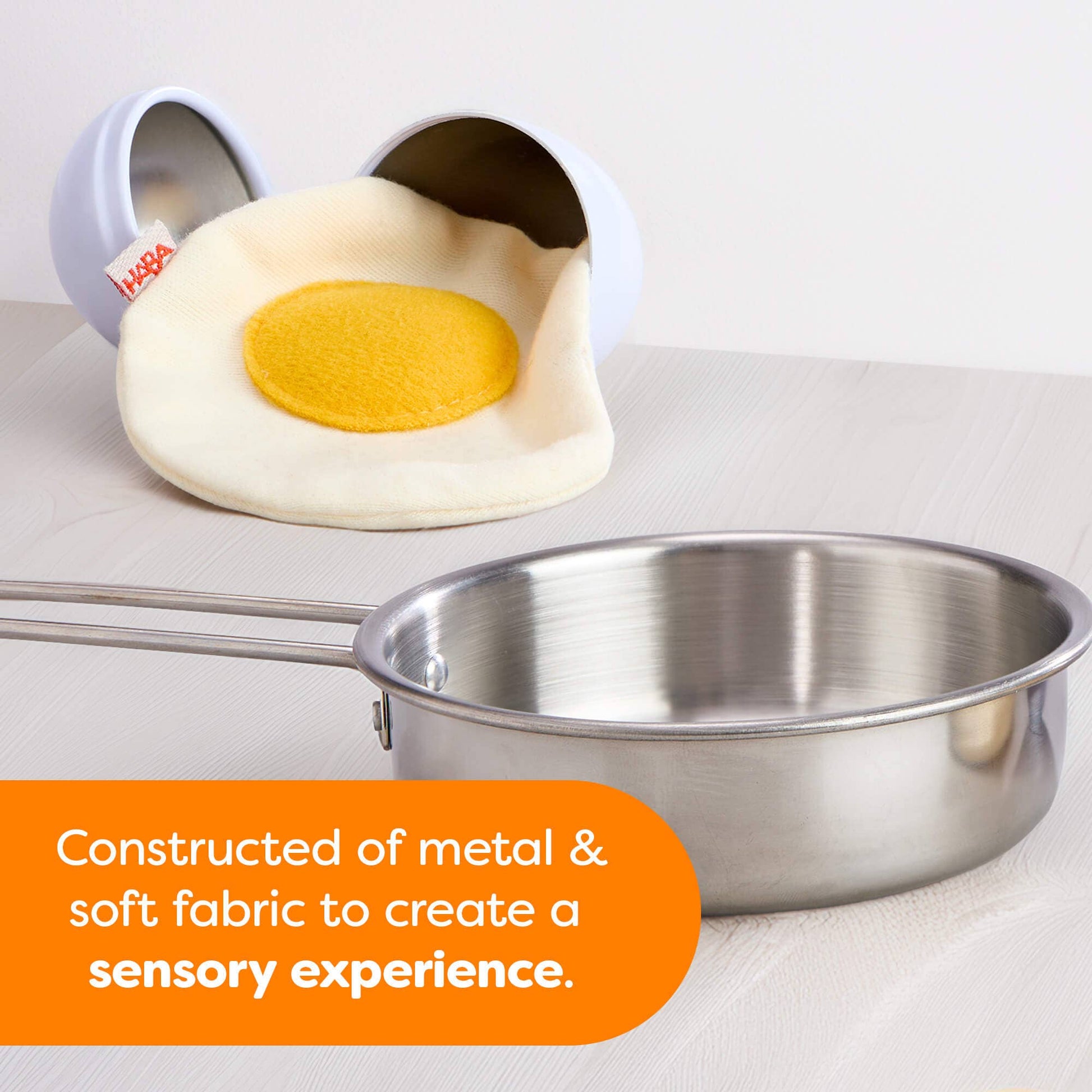 Toy shaped like a fried egg next to a metal pan on a white background