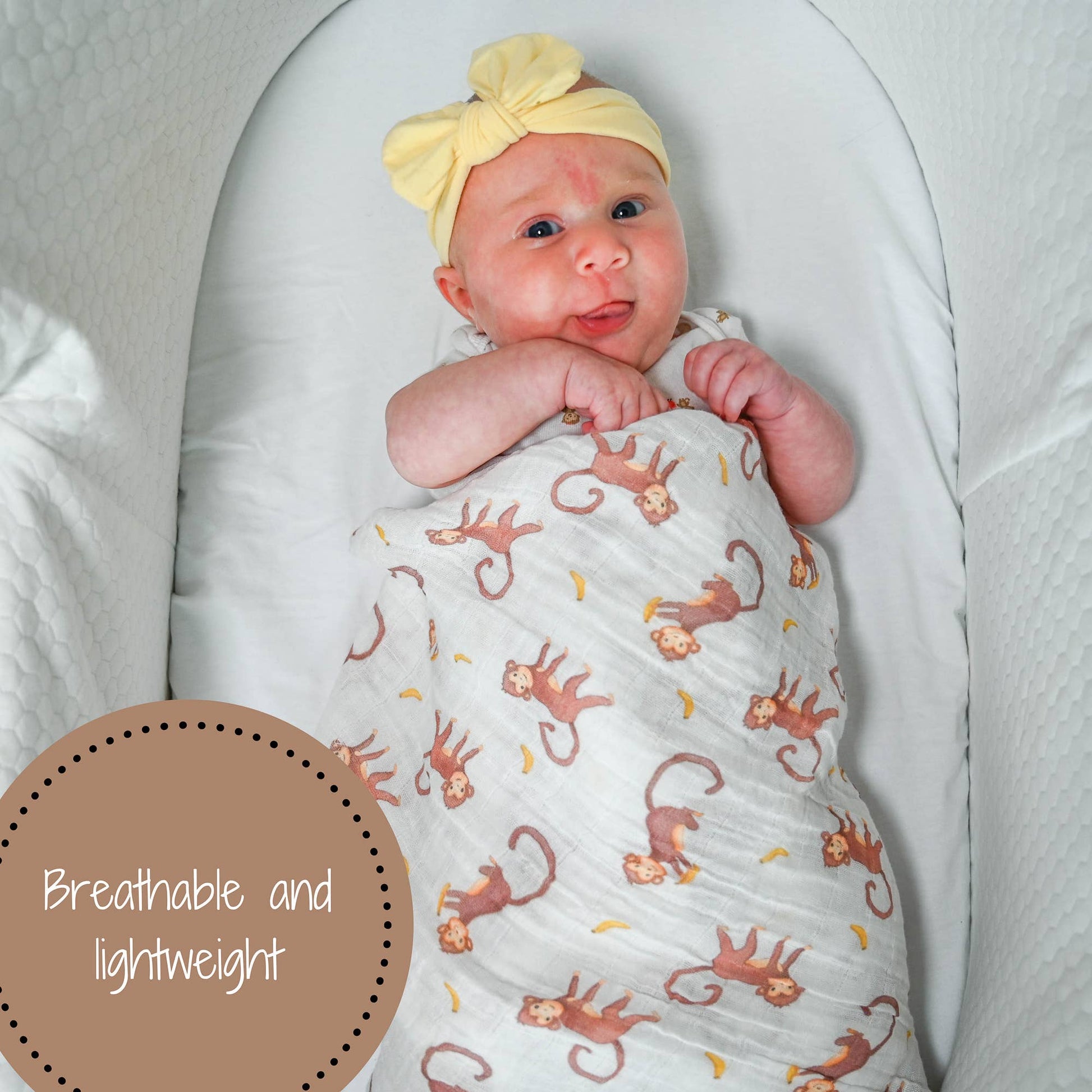 Baby wrapped in a blanket with monkey pattern, wearing a yellow headband, on a white background.
