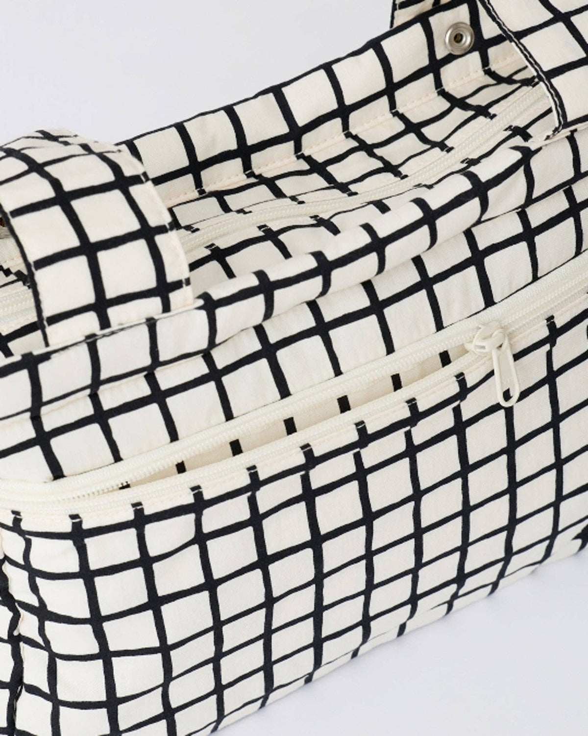 A close-up of a black and off-white grid patterned bag with a zipper pocket and top handle.