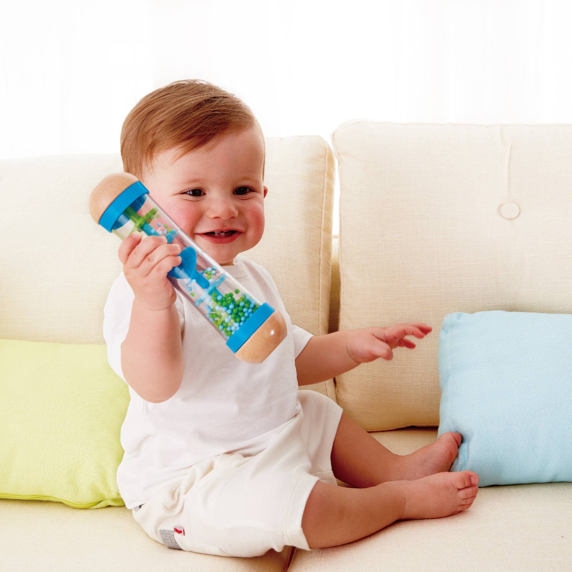 Baby sitting on a couch holding a colorful toy with a white background