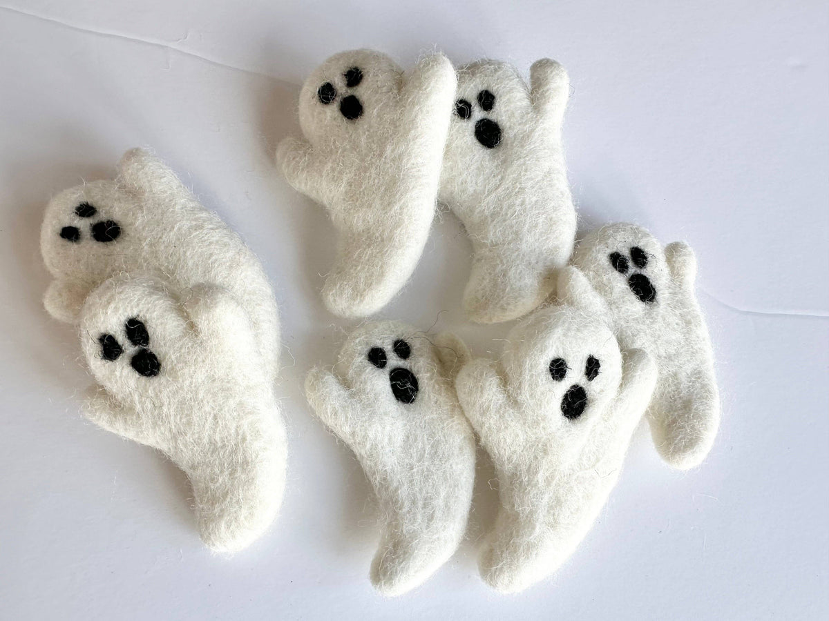 Five wet white felted wool ghost ornaments with black eyes and mouths, arranged on a plain white background.