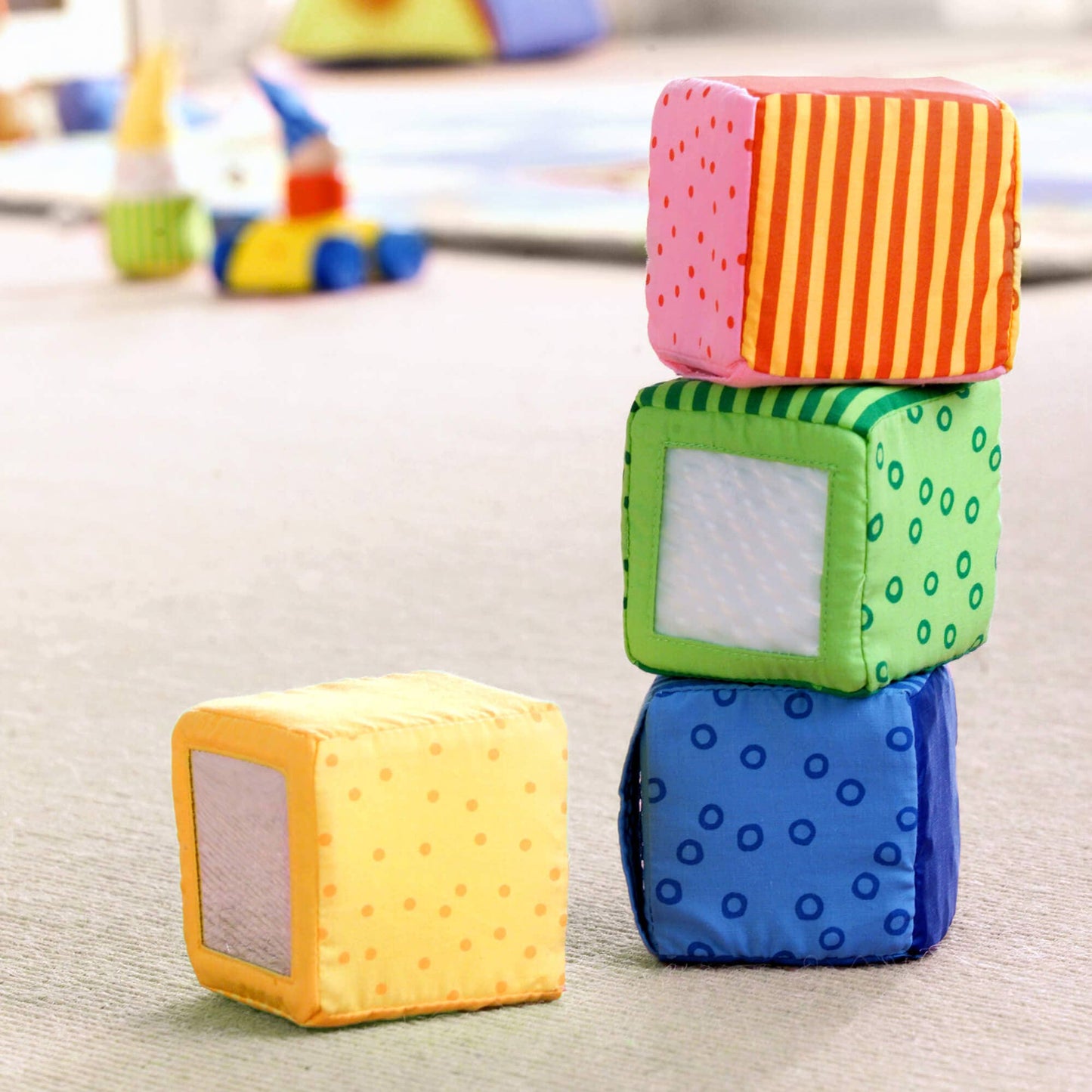 Colorful soft blocks stacked on a light surface with toys in the background