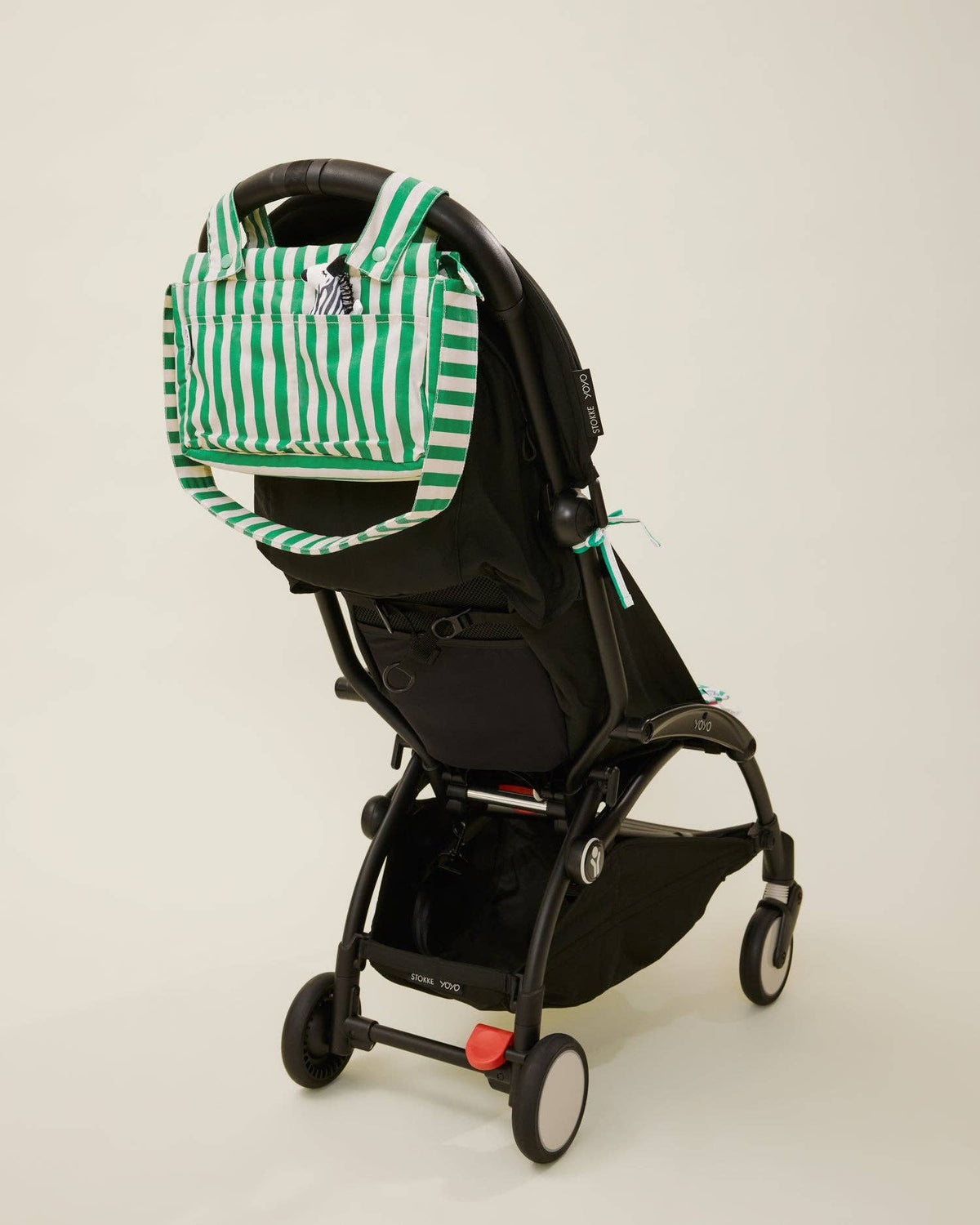 Black stroller with a green and white striped bag attached on a beige background