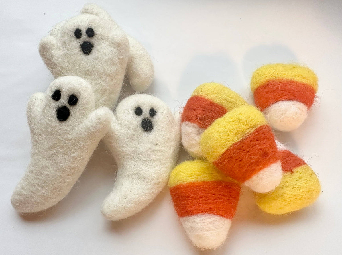 Felted Halloween decorations including three white ghost figures with black eyes and mouths, and several small candy corn pieces in yellow, orange, and white, arranged on a plain white background.