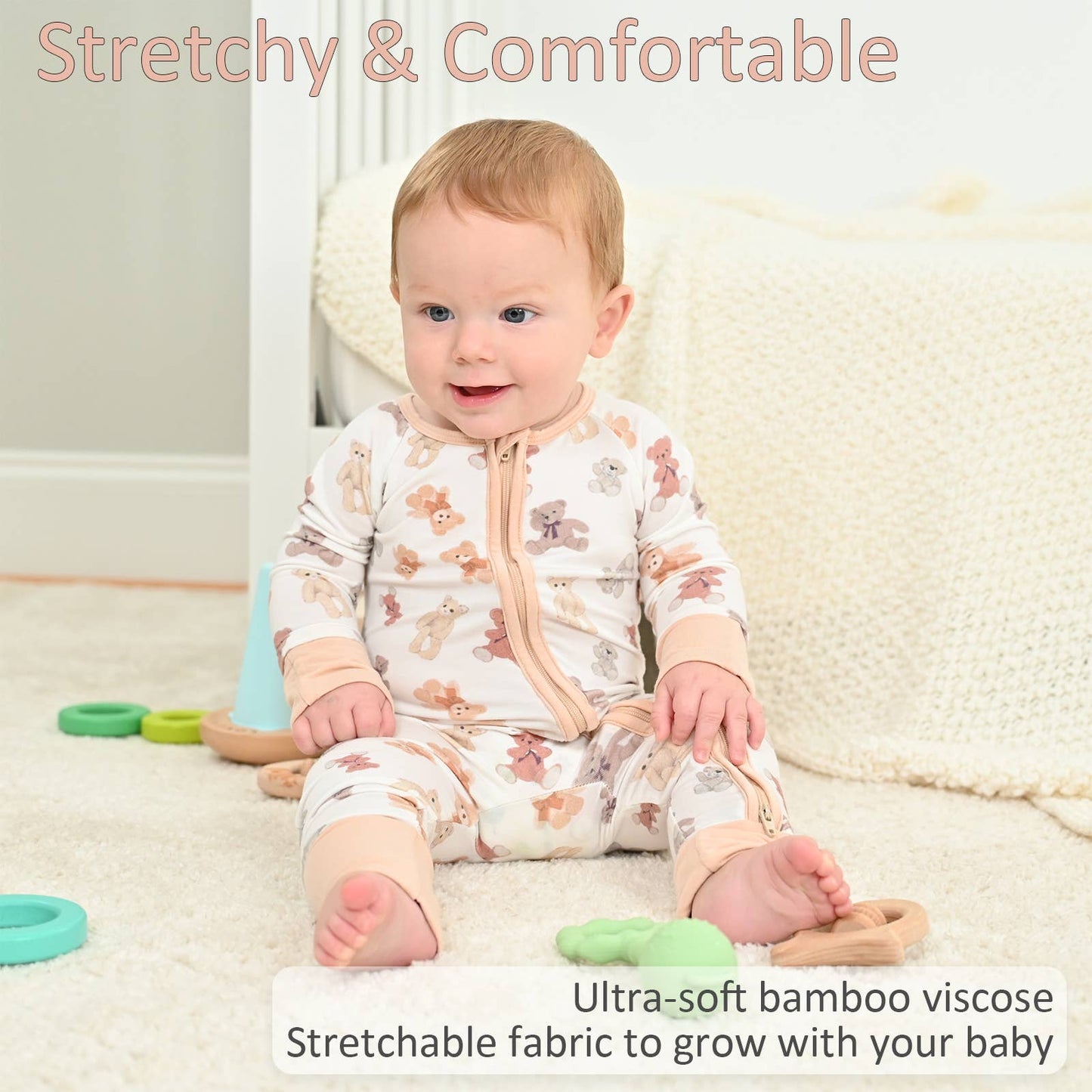 Baby wearing a teddy bear pajamas sitting on a carpeted floor with toys around.