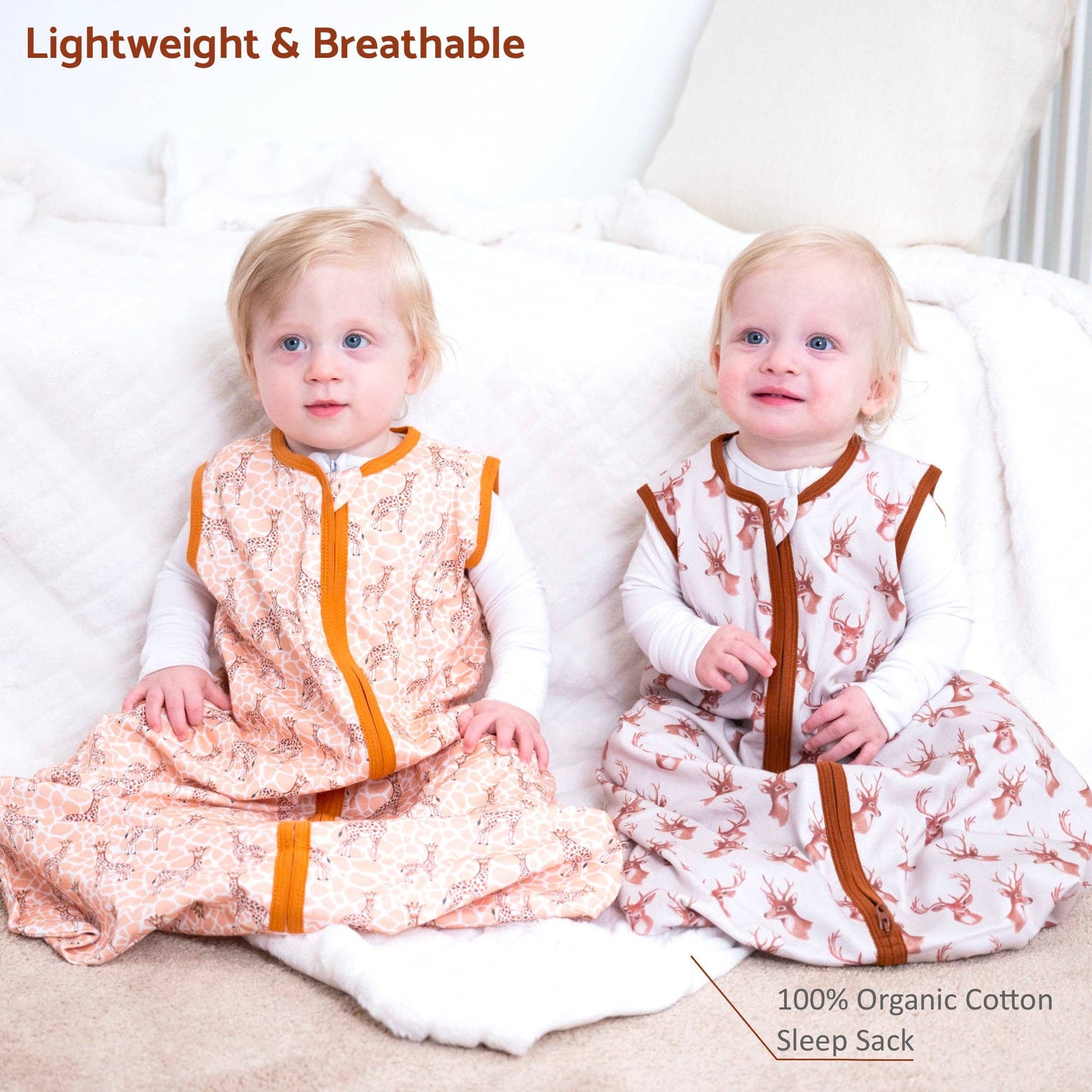 Two babies wearing organic cotton sleep sacks on a white couch.