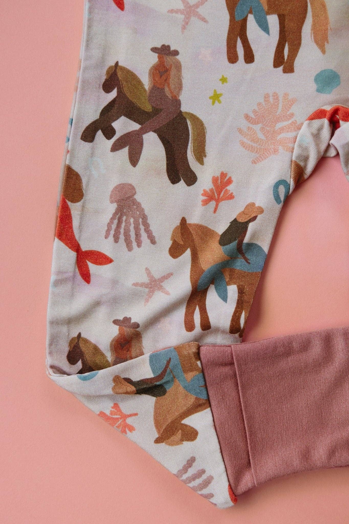 Patterned fabric with horses and mermaids on a pink background