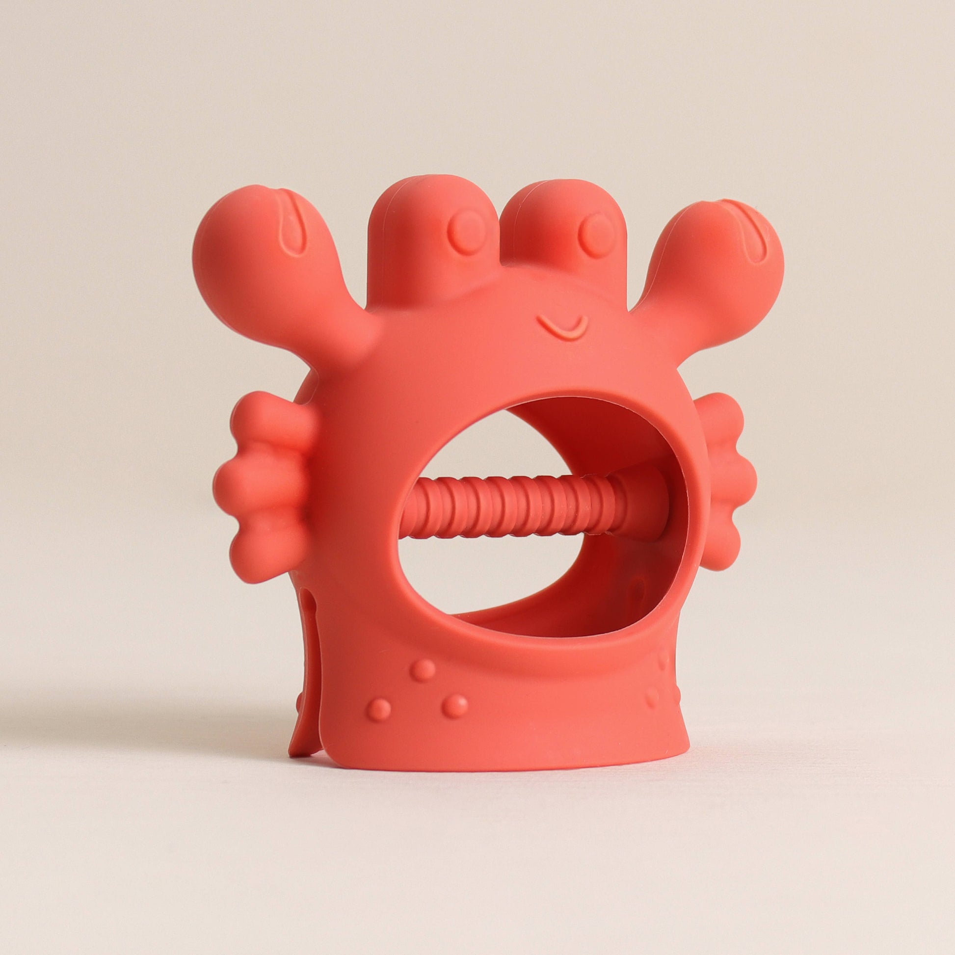 Red silicone teething ring with a smiling face on a beige background