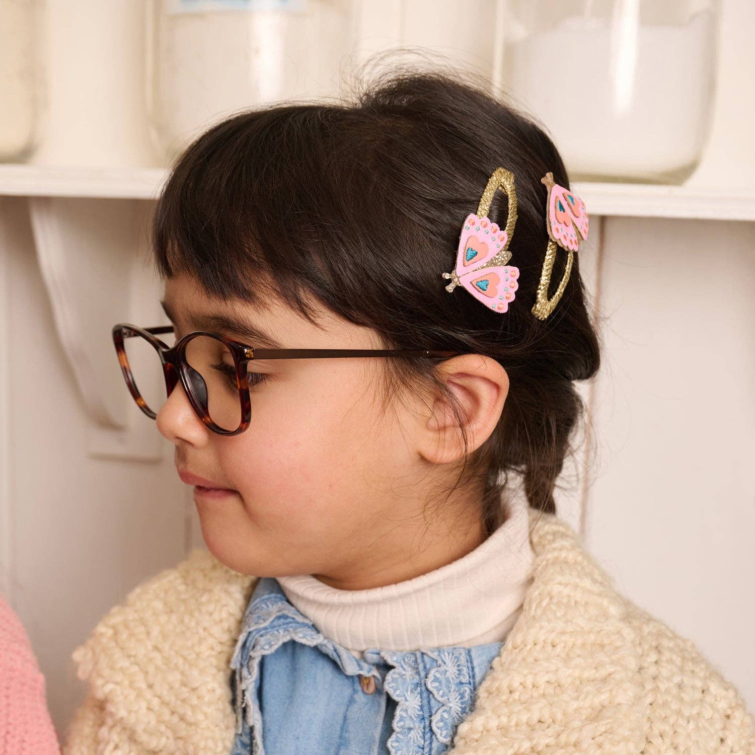 Child wearing glasses with decorative hair clips in a neutral setting