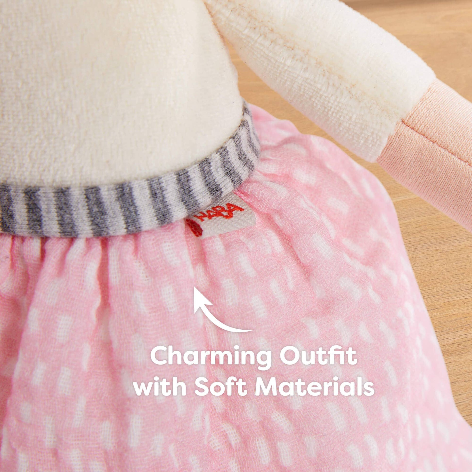 Close-up of a doll's outfit with a pink skirt and striped sweater, featuring a brand label.