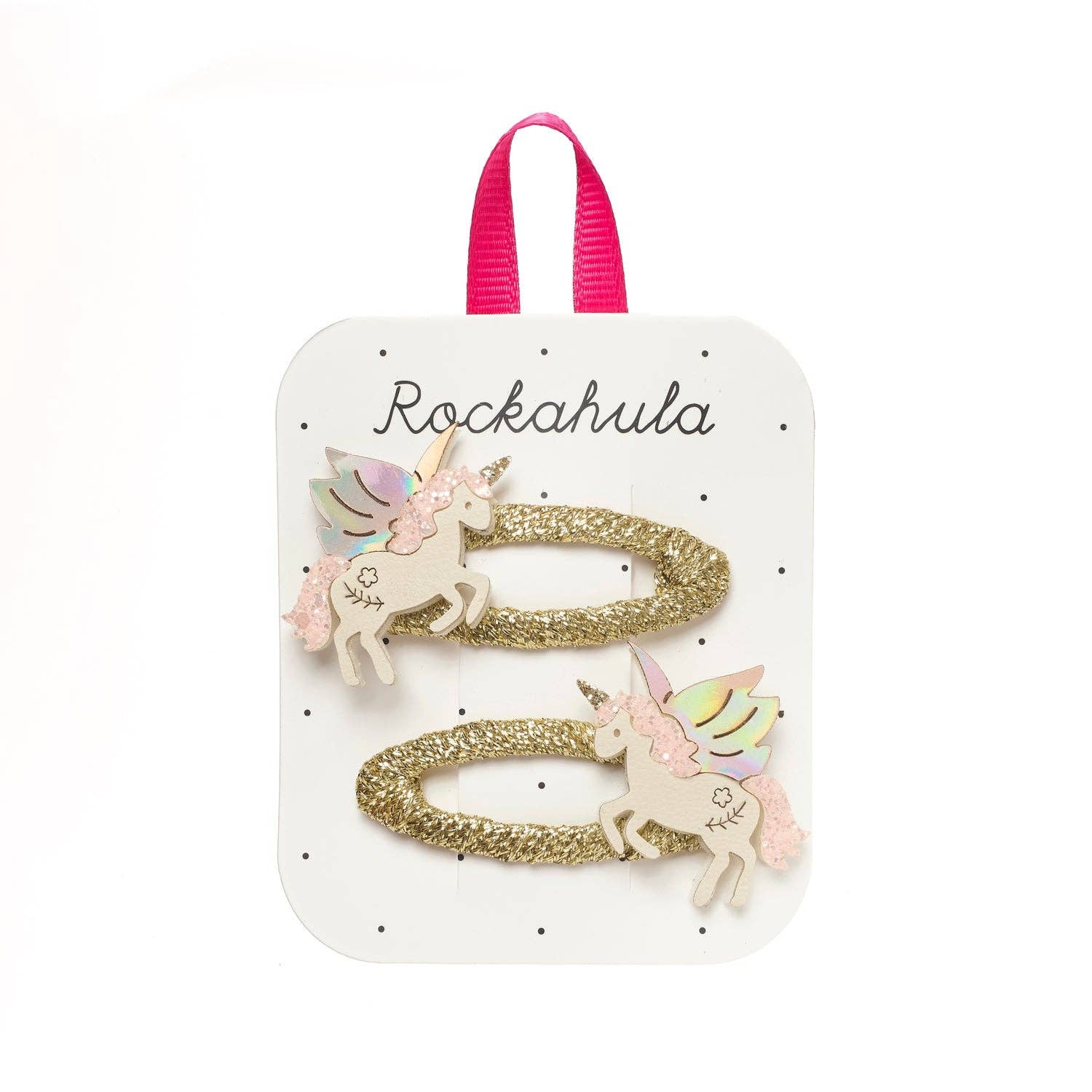 Two gold glitter unicorn hair clips with pastel wings and cream bodies, attached to a white display card with a pink ribbon loop. The card is branded 'Rockahula'.