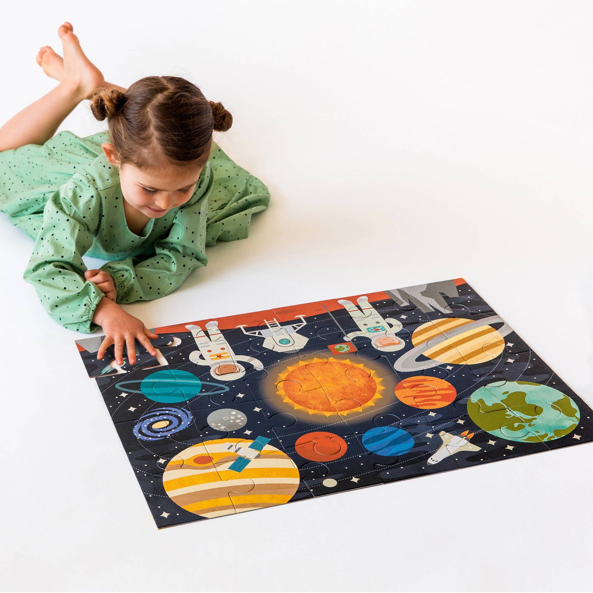 Child playing with a solar system puzzle on a white floor