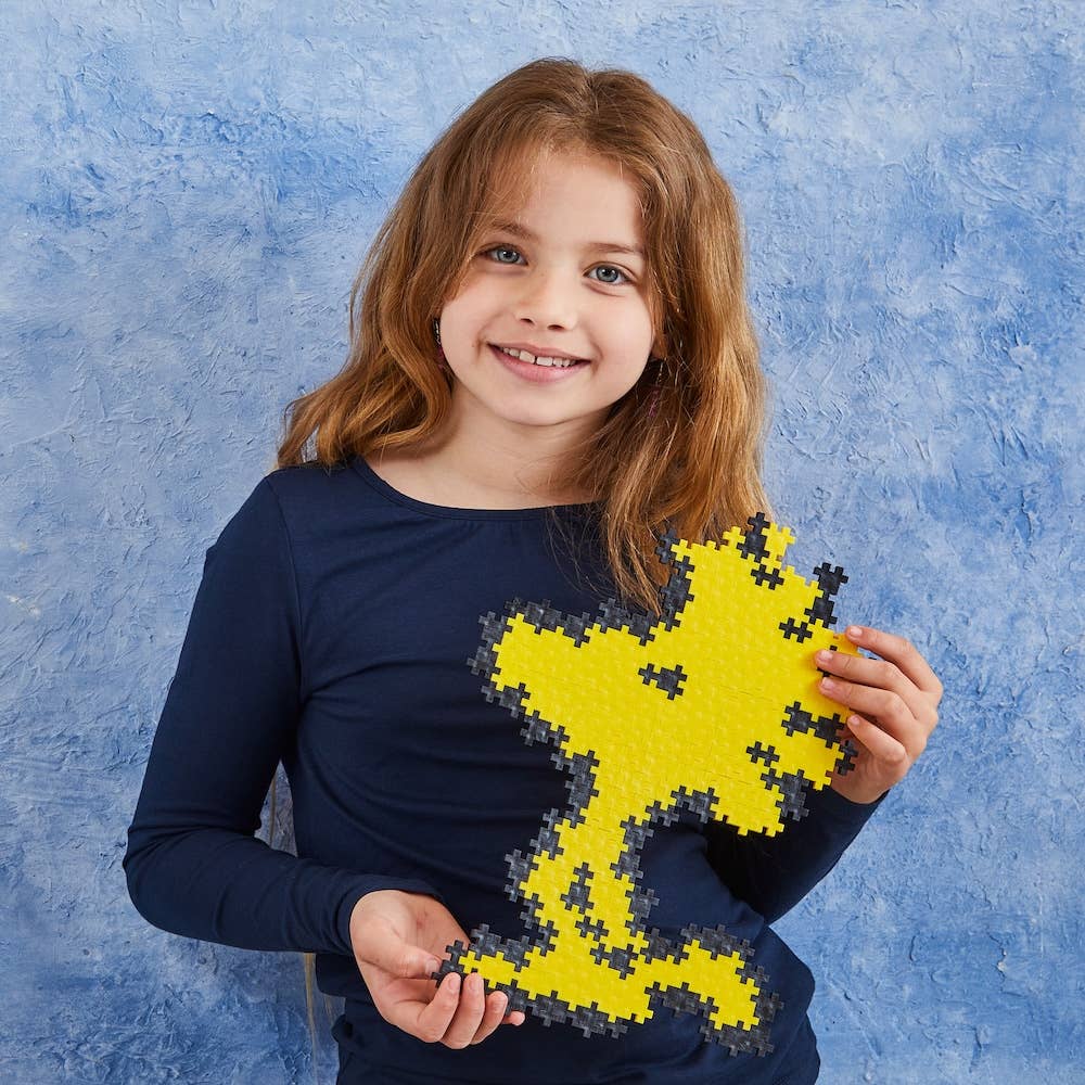 Young girl holding a yellow puzzle of Peanuts Woodstock against a blue background