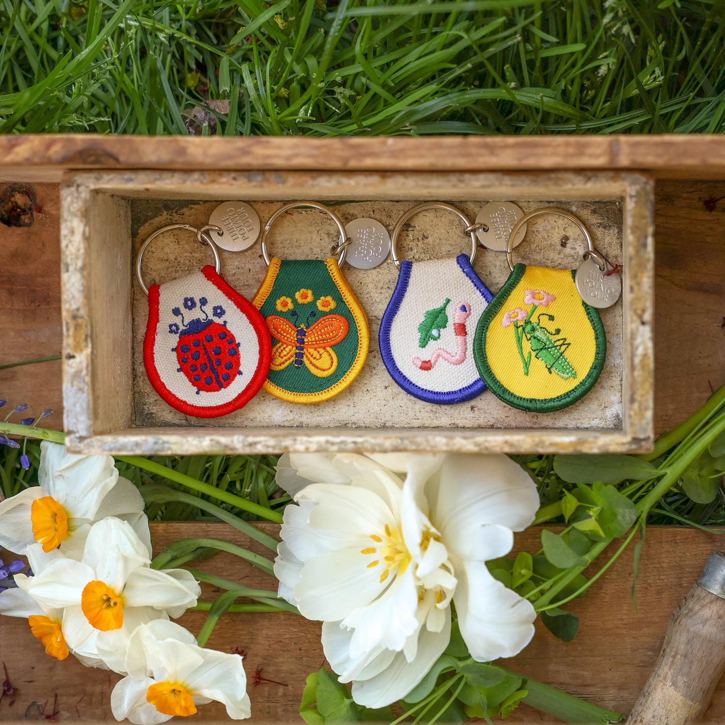 Set of colorful embroidered keychains in a wooden box with flowers and grass in the background