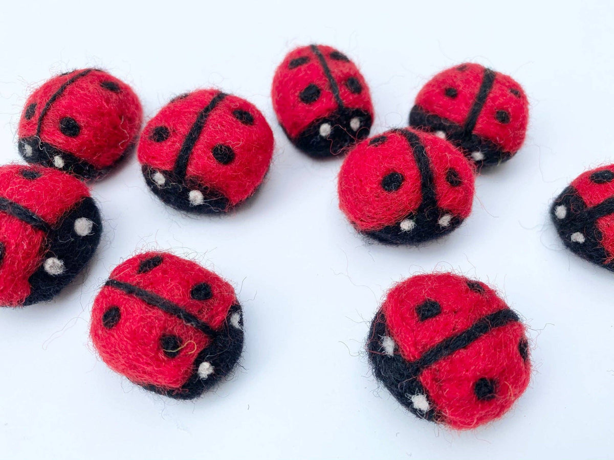 Red and black ladybug-shaped felted objects on a white background