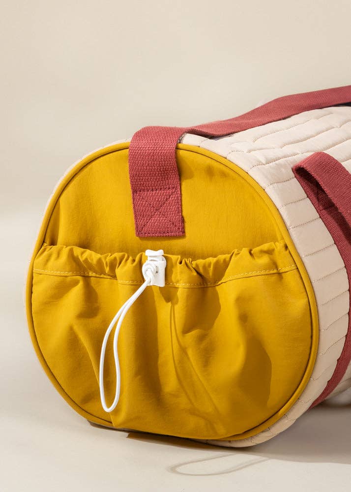 Yellow duffel bag with a red handle on a beige background