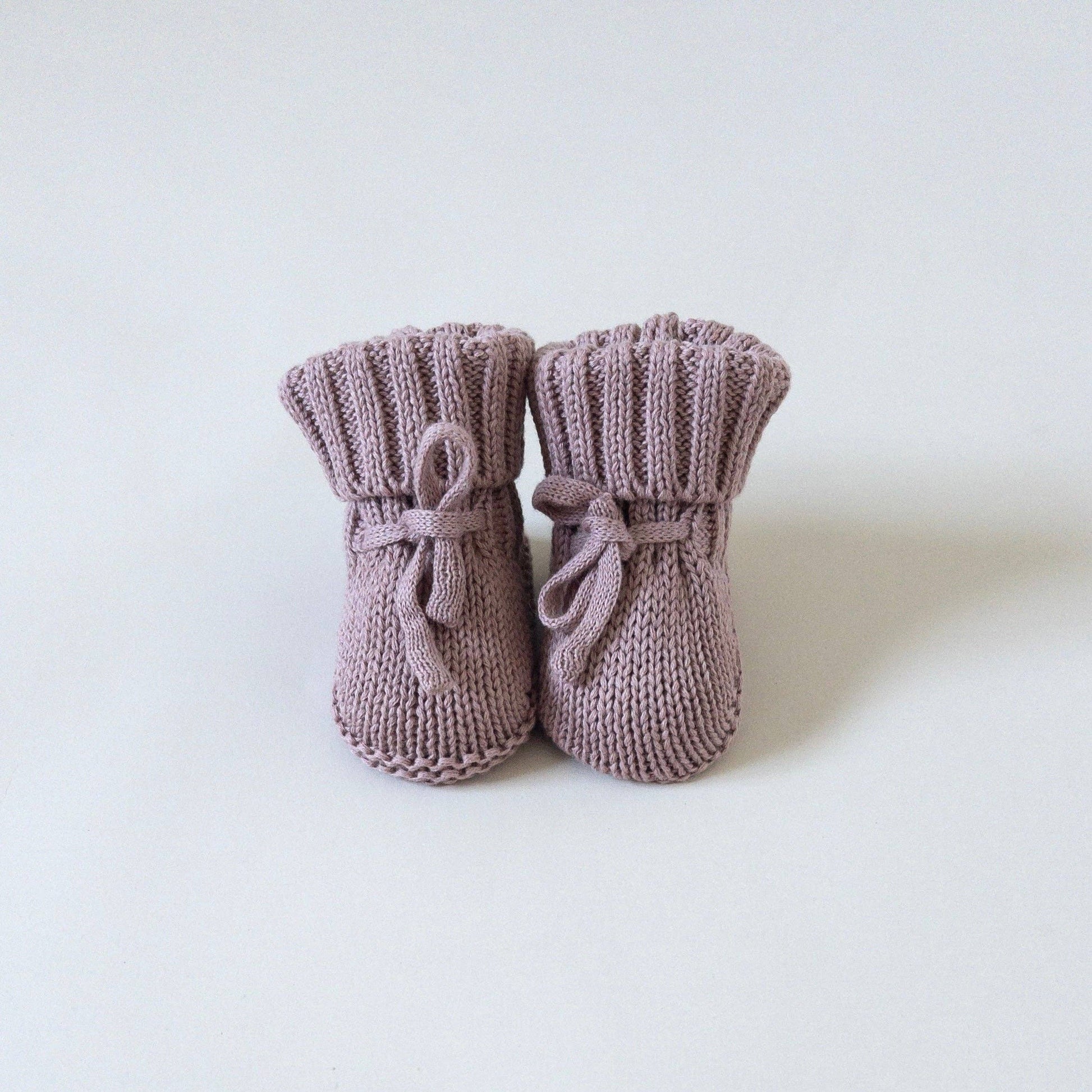 A pair of dusty mauve knit baby booties with matching fabric bows, displayed on a clean white background.
