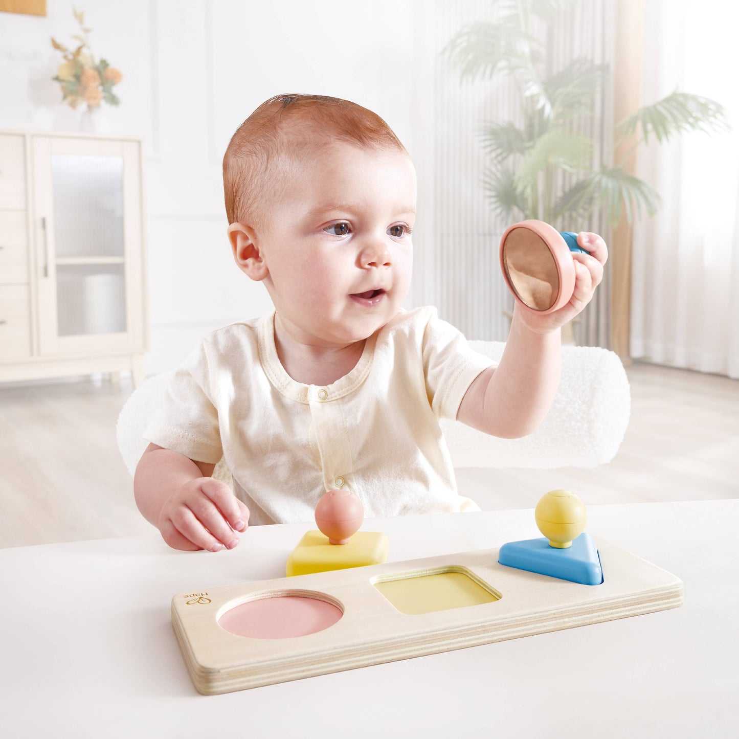 Baby playing with a wooden shape sorting toy in a bright room.